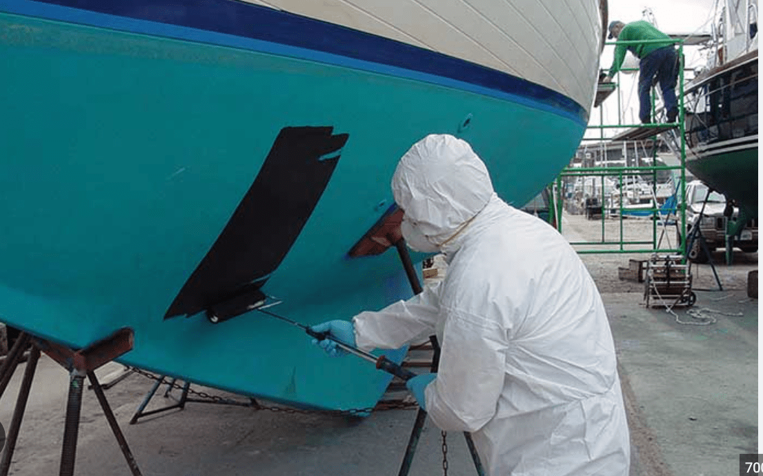 A person in white suit painting the hull of a boat.