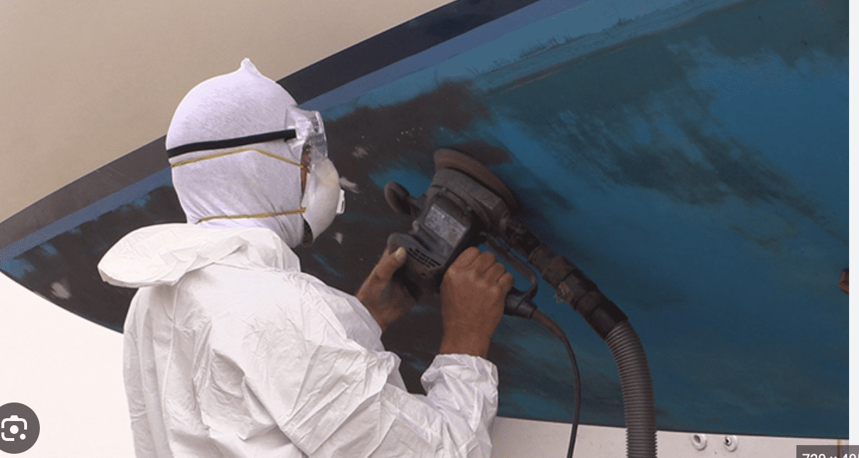 A person in white suit and mask using an electric sander.